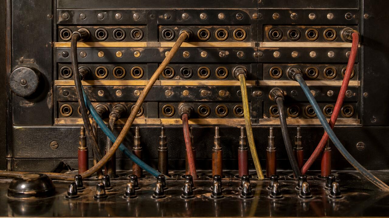 Un standard téléphonique ancien à fiches et cordons, des câbles de couleur reliant les prises d'un tableau de connexion en bakélite