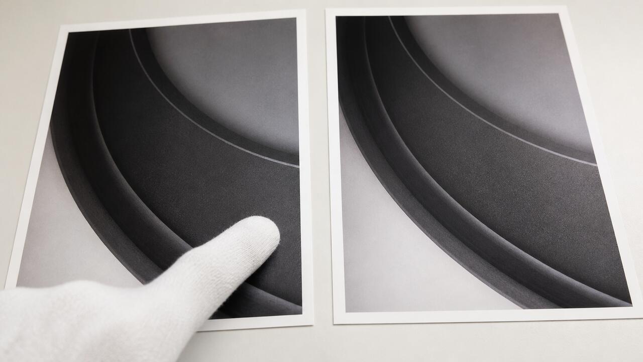 Deux tirages photographiques presque identiques posés côte à côte sur une table lumineuse, une main gantée désignant l'écart entre les deux