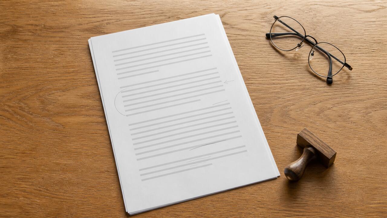 Un règlement imprimé posé sur une table en chêne, plusieurs paragraphes annotés au crayon gris, une paire de lunettes et un tampon en bois posés à côté